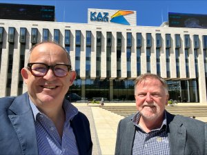 Two men in suits standing in front of an office building with blue sky in the background
