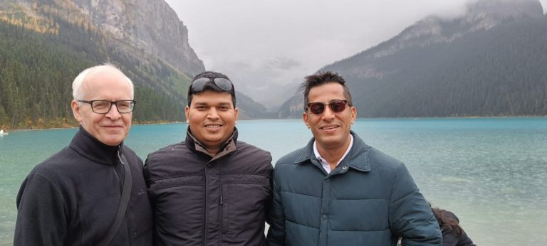 Three men standing in front of a blue lake and fjord in Canada